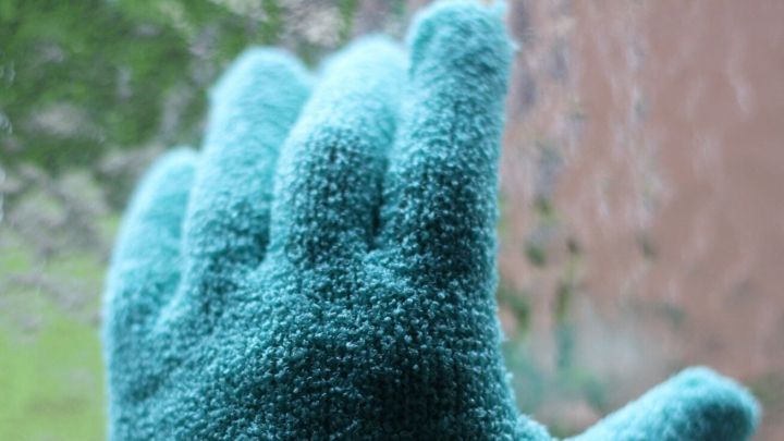 Eine gr&uuml;ne Handfl&auml;che eines Handschuhs wischt &uuml;ber eine beschlagene Fensterscheibe voller Fliegendreck.