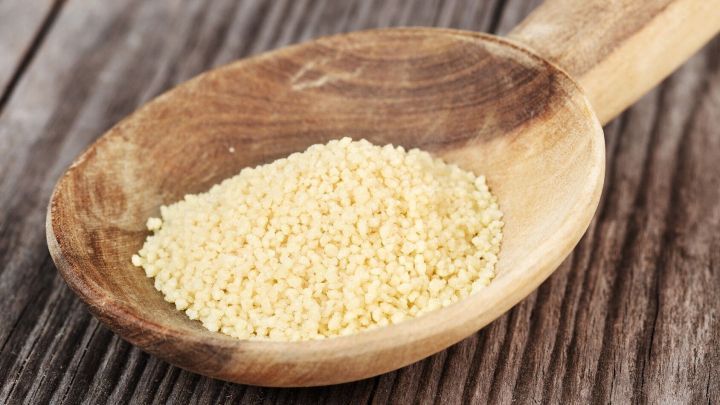 Eine Holzschaufel enth&auml;lt feinen Couscous, der auf einer rustikalen Holzoberfl&auml;che liegt, bereit zur Zubereitung.