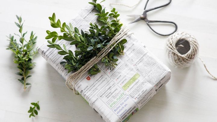 Ein sch&ouml;n verpacktes Geschenk in Zeitungspapier liegt auf einem Tisch, dekoriert mit frischen Zweigen und Schnur.
