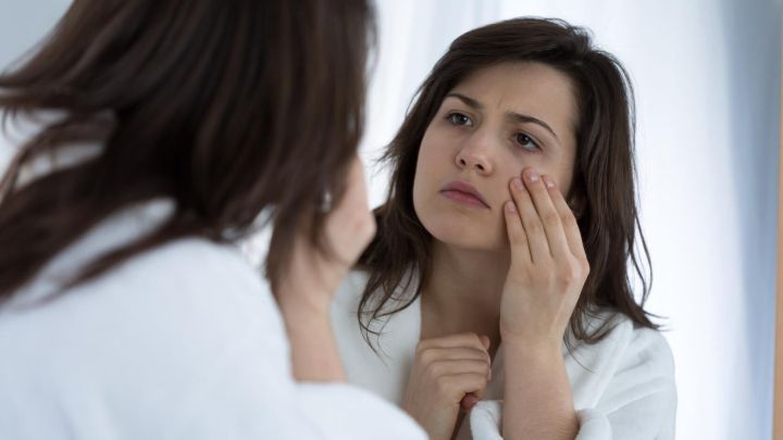 Eine Frau betrachtet ihre Augenringe im Spiegel, w&auml;hrend sie sanft ihre Haut ber&uuml;hrt, um die Wirkung von Kaffeepads zu testen.