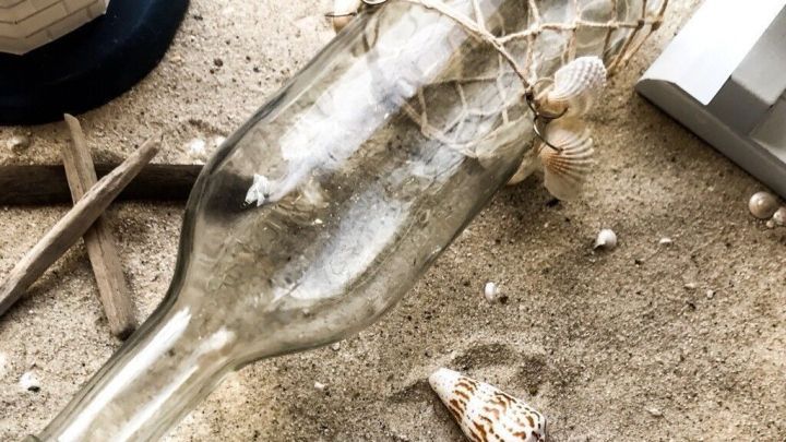 Eine dekorative Flasche liegt im Sand, umgeben von Muscheln, ideal f&uuml;r Dekosand-Projekte in maritimem Stil.