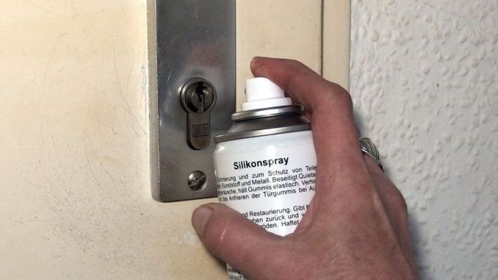 Eine Hand spr&uuml;ht Schmiermittel in einen Schlie&szlig;zylinder an einer T&uuml;r, um dessen Funktion zu verbessern.