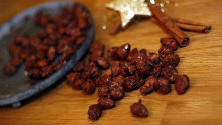 Gebrannte Mandeln liegen verstreut auf einem Holztisch, umgeben von einer Zimtstange und einem glitzernden Stern.