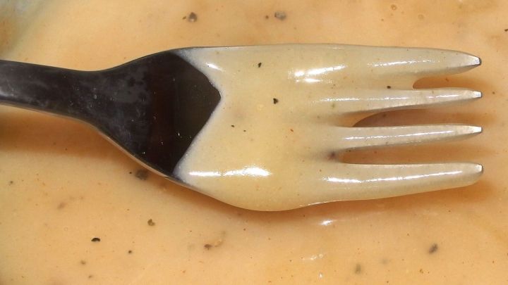 Eine Gabel liegt in einer fettreduzierten Sahnesauce, die cremig und leicht beige ist, umgeben von einem neutralen Hintergrund.