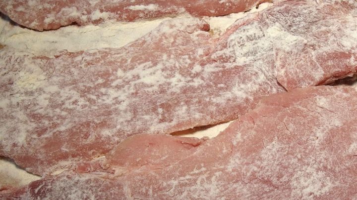 D&uuml;nne Fleischscheiben liegen mit Mehl best&auml;ubt auf einer Arbeitsfl&auml;che, bereit zum Panieren in der K&uuml;che.