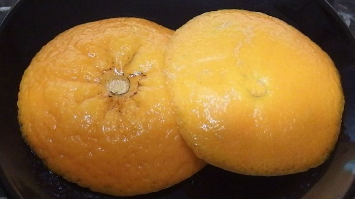 Zwei orangefarbene Zitrusschalen liegen &uuml;bereinander auf einem schwarzen Teller, bereit zur Dekoration und kreativen Verwendung.