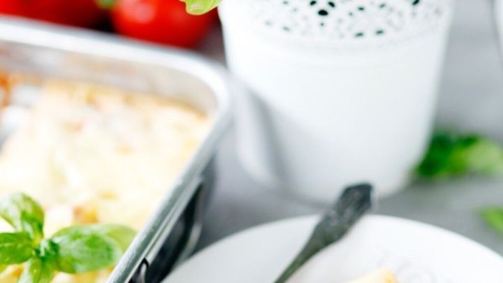 Ein Teller mit Bolognese-Lasagne liegt neben einer Auflaufform und frischem Basilikum in einem Topf, umgeben von Tomaten.