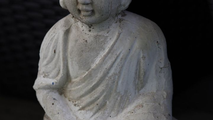 Eine Buddha-Statue sitzt ruhig im Schneidersitz auf gr&uuml;nem Untergrund und strahlt Entspannung und Gelassenheit aus.