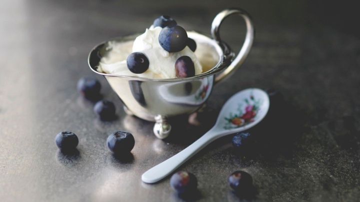 Ein silbernes Sch&auml;lchen mit Eis und Blaubeeren wird auf einer dunklen Oberfl&auml;che pr&auml;sentiert, umgeben von frischen Blaubeeren.