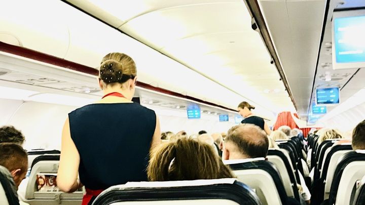 Eine Flugbegleiterin bewegt sich durch den Gang eines Flugzeugs, w&auml;hrend Passagiere in ihren Sitzen sitzen.