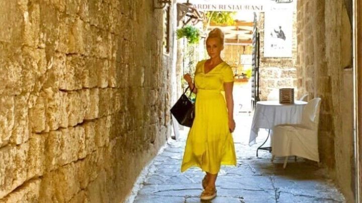 Eine Frau in einem gelben Kleid l&auml;uft durch einen schmalen, steinernen Gang, umgeben von alten Mauern und Licht.