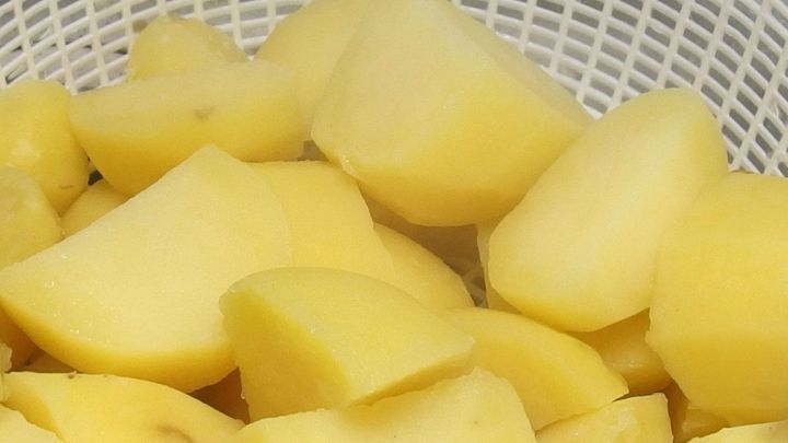 Abgie&szlig;en: Ein Sieb enth&auml;lt gekochte, gelbe Kartoffelst&uuml;ckchen, bereit zum Servieren in einer K&uuml;chenumgebung.