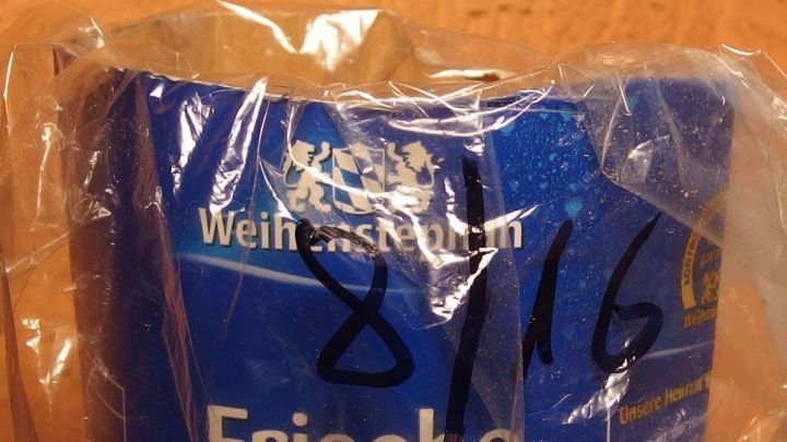 Ein blauer Beh&auml;lter mit der Aufschrift &bdquo;Frische&ldquo; steht umh&uuml;llt von Folie auf einer Holzoberfl&auml;che.