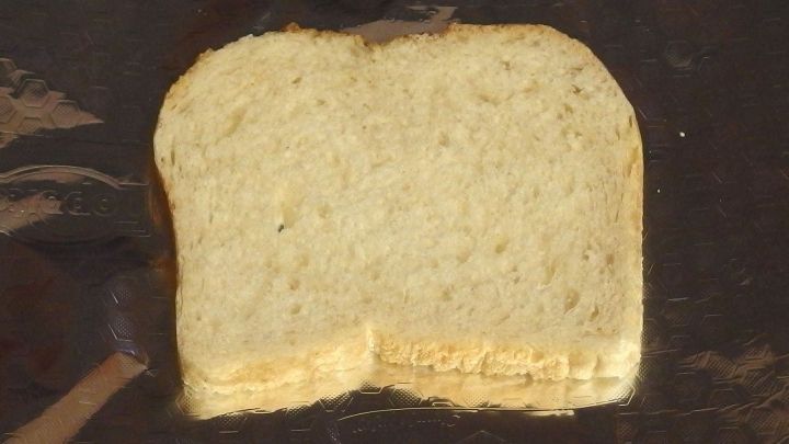 Ein St&uuml;ck Toastbrot liegt flach auf einem dunklen Tisch, bereit, ohne Toaster zubereitet zu werden.