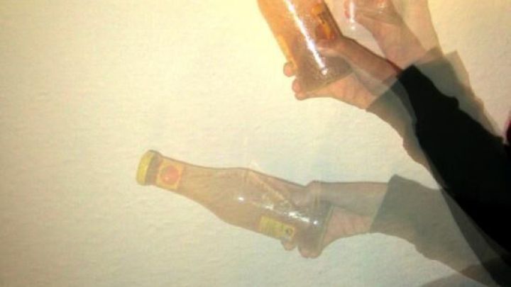 Eine Ketchupflasche wird in mehreren Bewegungen geschwenkt, um die (Zentrifugal-)Kraft zu nutzen, vor einer hellen Wand.