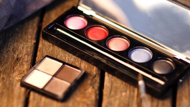 Eine Lidschattenpalette mit verschiedenen Farben liegt auf einer Holztischoberfl&auml;che, umgeben von einem nat&uuml;rlichen, warmen Licht.