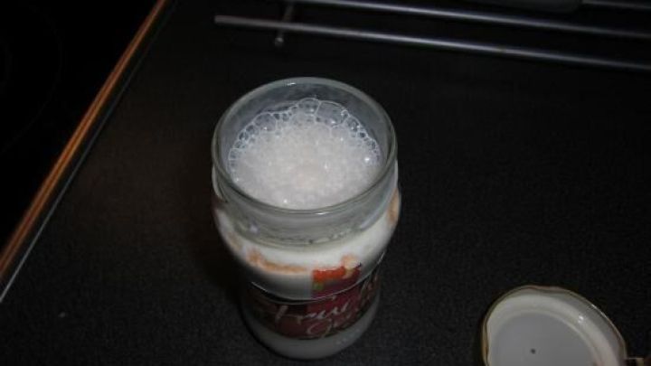 Ein Marmeladenglas steht offen auf einer K&uuml;chenarbeitsplatte, gef&uuml;llt mit einem schaumigen Milchshake.