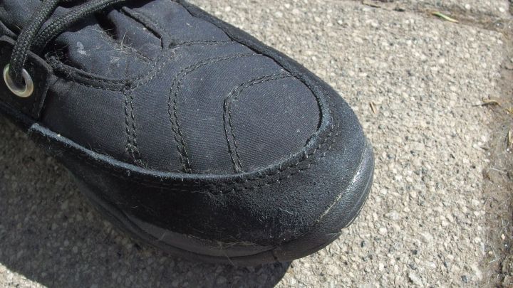Ein schwarzer Schuh mit sichtbaren Salzr&auml;ndern liegt auf einem grauen, steinernen Untergrund in einem sonnigen Umfeld.