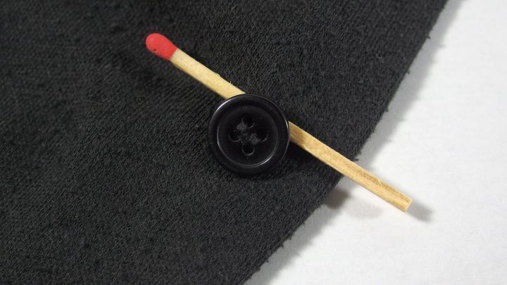 Ein schwarzer Stoff mit einem Knopf und einem roten Streichholz, das quer &uuml;ber den Stoff gelegt ist.
