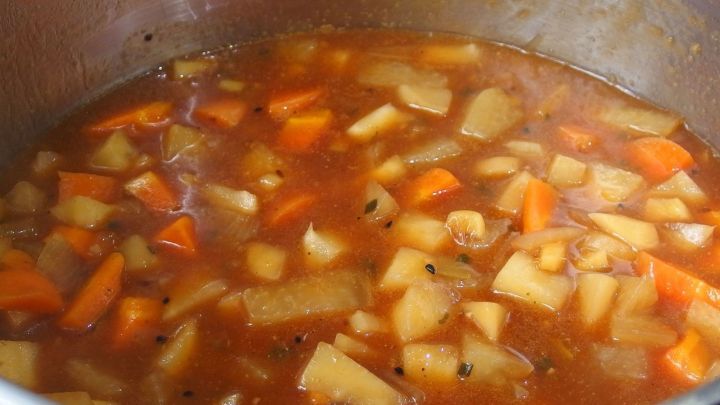 Eine dampfende, aromatische Suppe aus Kartoffeln und Gem&uuml;se k&ouml;chelt in einem Topf, umgeben von einer herzlichen K&uuml;chenatmosph&auml;re.