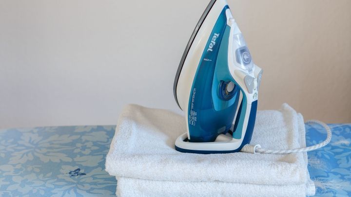Ein Dampfb&uuml;geleisen steht auf einem gestapelten Handtuch, bereit, Kleidung zu b&uuml;geln, vor einem hellen Hintergrund.