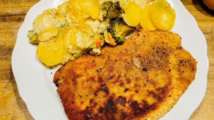 Eine goldbraun panierte Zwieback-Schnitzel-Portion liegt auf einem Teller, umgeben von cremigen Kartoffeln und Gem&uuml;se.