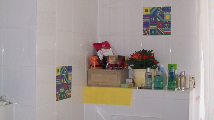 In einem Badezimmer mit wei&szlig;en Fliesen steht eine Ablage voller Pflegeprodukte und Pflanzen, umgeben von hellen W&auml;nden.