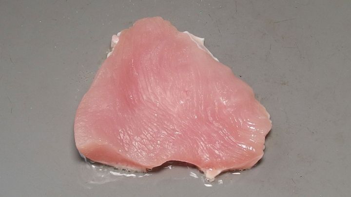 Ein St&uuml;ck rohes H&uuml;hnerfleisch liegt auf einer flachen Oberfl&auml;che, bereit zum Braten in der K&uuml;che.