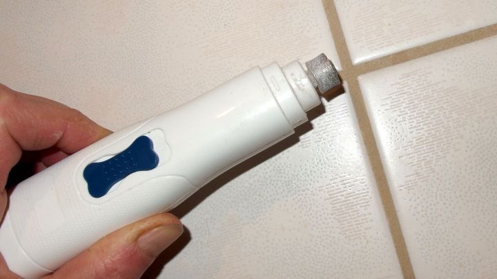 Ein Dremel wird in der Hand gehalten, um Schimmel in den Fugen einer hellen Fliese zu entfernen.