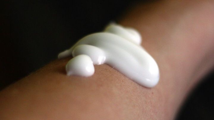 Eine handvoll Sonnenschutzmittel mit hohem UV-Schutz wird auf die Haut eines Arms aufgetragen, um vor Sonne zu sch&uuml;tzen.