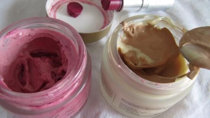 Zwei offene T&ouml;pfe mit get&ouml;nter Tagescreme und Rouge, w&auml;hrend ein L&ouml;ffel in die Creme eingetaucht wird.