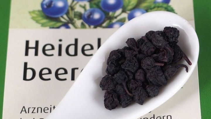 Getrocknete Heidelbeeren liegen in einem L&ouml;ffel auf einer Verpackung, die Informationen &uuml;ber ihre Verwendung bei Durchfall bietet.