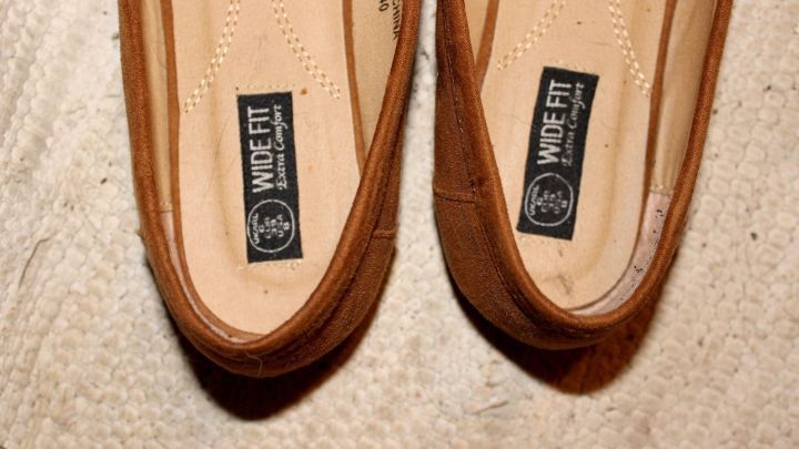 Braune Schuhe liegen auf einem Teppich, zeigt die Ferse, die an der Innenseite scheuert, w&auml;hrend das Problem sichtbar wird.