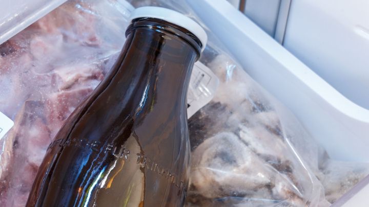 Eine braune Flasche steht in einem Gefrierfach, umgeben von gefrorenem Fleisch, das ordentlich verstaut ist.