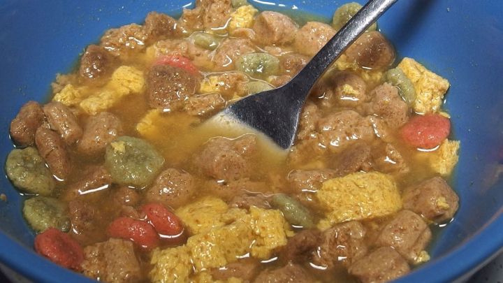 Ein blauer Teller voller Mischkost, der mit einem L&ouml;ffel umger&uuml;hrt wird, w&auml;hrend die Zutaten in einer herzhaften Br&uuml;he schwimmen.