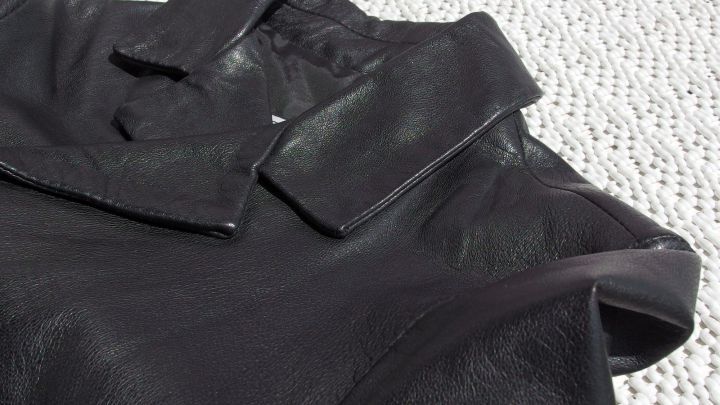 Ein speckiger Lederjackenkragen liegt auf einem hellen Untergrund, bereit, mit einem Erfrischungstuch gereinigt zu werden.