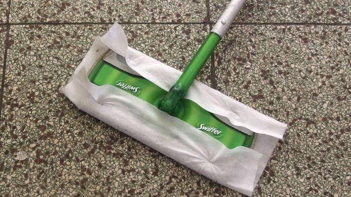 Ein Swiffer liegt auf einem grauen Fliesenboden, bereit zum Reinigen, mit einem frischen Reinigungstuch.