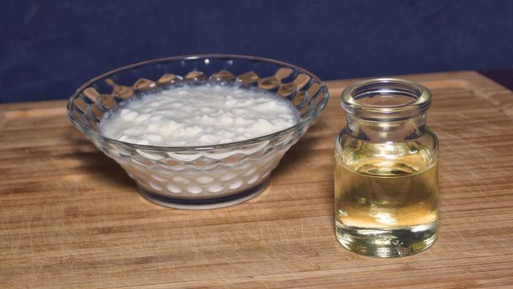 Ein Sch&auml;lchen Quark steht neben einer Flasche mit Lein&ouml;l auf einem Holzbrett. Die Szene ist einfach und rustikal.