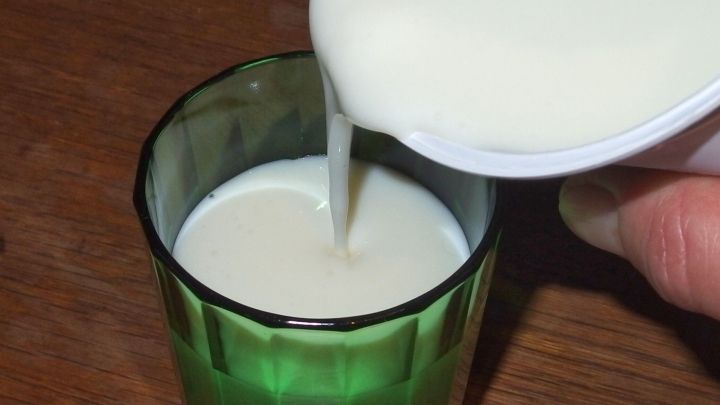 Eine Hand gie&szlig;t k&uuml;hle Milch in ein gr&uuml;nes Glas, um eine Erholung nach einem Gaumen verbrannt zu erm&ouml;glichen.