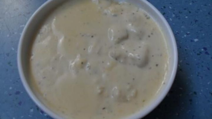 Eine cremige Sherry-Blumenkohl-So&szlig;e in einer wei&szlig;en Schale steht auf einem blauen Tisch. Sie wirkt einladend und frisch.