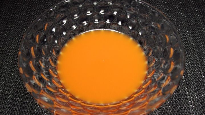 Ein tiefes Sch&uuml;sselchen mit leuchtend orangefarbigem Saft steht auf einer dunklen Oberfl&auml;che und reflektiert sanft das Licht.