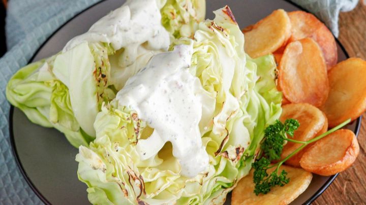 Gebratener Spitzkohl ist auf einem Teller mit cremigem Dressing und goldbraunen Kartoffeln serviert.