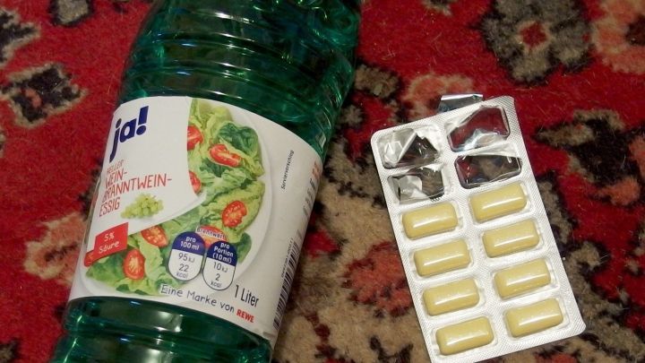 Eine Flasche Essig liegt auf einem Teppich neben einer Packung Kaugummitabletten, bereit zur Fleckenentfernung.