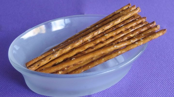 Knusprige Salzstangen liegen in einer klaren Schale auf einem lila Tisch, bereit zum Snacken.