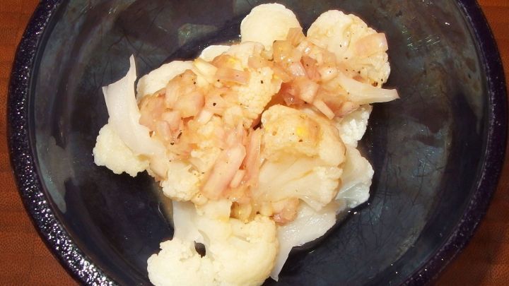 Blumenkohl mit gehackten Zwiebeln in einer dunklen Schale, serviert auf einem Holztisch.