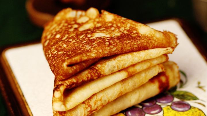 Ein Stapel goldbrauner Cr&ecirc;pes liegt auf einem dekorativen Teller mit frischen Obstmotiven, bereit zum Essen.