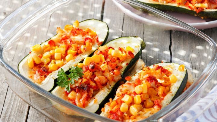 Gef&uuml;llte Zucchini liegen in einer Glasform, &uuml;berbacken mit Gem&uuml;se und K&auml;se, auf einem rustikalen Holztisch.