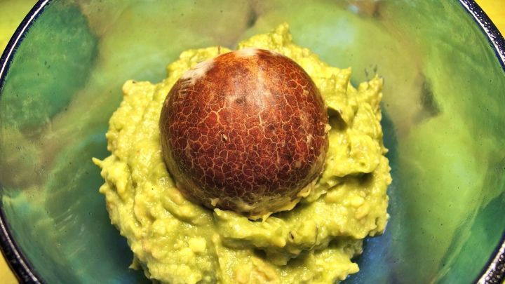 Eine gr&uuml;ne Guacamole liegt in einer Sch&uuml;ssel, w&auml;hrend ein Avocadokern in der Mitte platziert ist, um Braunwerden zu verhindern.