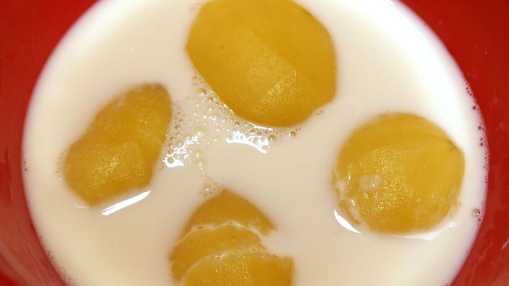Gelbe Kartoffeln schwimmen in einer roten Sch&uuml;ssel mit Milch, um f&uuml;r Kartoffelsalat eingelegt zu werden.