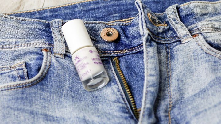 Ein Fl&auml;schchen Nagellack liegt auf einer Jeans mit Metallknopf, um eine Nickelallergie zu vermeiden.
